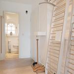 Flur mit Holzdielen, Bad mit Toilette und Fenster, Holzregale an der Wand.