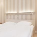 Schlafzimmer mit Bett, Nachttisch und gestreifter Wand