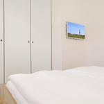 Schlafzimmer mit weißem Bett, Kleiderschrank und Wandbild
