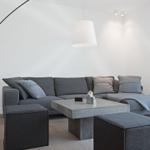 Ein Wohnzimmer mit grauem Sofa, Beton-Tisch und schwarzer Bogenlampe.