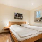 Schlafzimmer mit Doppelbett, Holzrahmen, Fenster und Wandbild.