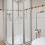 Duschkabine mit Glaswand, Toilette und Toilettenpapierhalter an Wand.