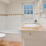 Badezimmer mit Badewanne, Waschbecken und Toilette. Fenster mit Jalousie.
