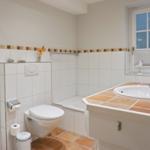 Badezimmer mit Toilette, Waschbecken und Dusche. Fenster mit Jalousie.