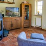 Wohnzimmer mit Kamin, Fernseher und Holzmöbeln auf Terrakottboden.