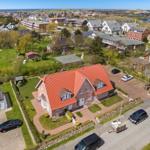 Haus mit rotem Dach und Garten. Mehrere Autos auf dem Hof. Blick auf die Ortschaft und das Meer.