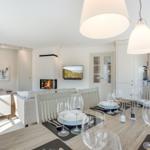 Essbereich mit Tisch und Stühlen, Wohnbereich mit Sofa und Kamin, Küche im Hintergrund.