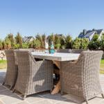 Terrasse mit Esstisch und sechs Stühlen. Hintergrund: Garten, Steinmauer und Häuser.