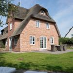 Rotes Backsteinhaus mit Strohdach, Terrasse und Garten mit Liegestühlen.
