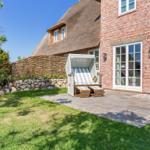 Haus mit strohgedecktem Dach und Steinmauer im Garten mit Liegestuhl.