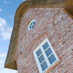 Rotes Ziegelhaus mit Strohdach und Fenstern unter blauem Himmel.