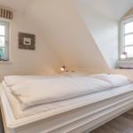 Bedroom with double bed, two windows, and wooden floor.