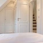 Bedroom with white bed and wardrobe under sloped ceiling. Door leads to stairs.