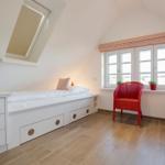 Bedroom with sloped ceiling, bed, TV, and red seating.