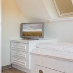 Bedroom with bed, dresser, and TV under sloped ceiling.