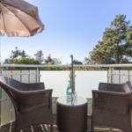 Terrace with two chairs, table, and umbrella. View of trees and sky.