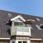 Attic level with balcony and umbrella under blue sky.
