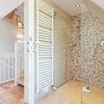 Dusche mit Mosaikwand, Heizkörper und angrenzender Treppe.