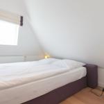 Schlafzimmer mit Doppelbett, Fenster und Nachttisch mit Lampe.