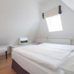 Schlafzimmer mit Doppelbett, Stuhl und Fenster unter Dachschräge.