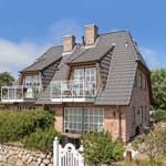 Haus mit Balkon, Terrasse und Garten. Steinmauer und weiße Zaun.