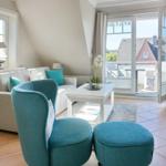 Wohnzimmer mit Sofa, blauem Sessel und Terrasse. Blick auf Dächer und Garten.