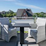 Terrasse mit zwei Stühlen und Tisch. Blick auf Häuser und Grünflächen.