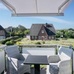 Terrasse mit Tisch und Stühlen. Blick auf Häuser und Grünflächen.
