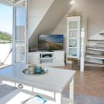 Wohnzimmer mit TV, Glasvitrine und Terrasse. Holztreppe und Terrassenmöbel sichtbar.