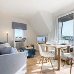 Wohn- und Essbereich mit Sofa, Tisch und Stühlen. Glastür führt auf Balkon mit Blick.