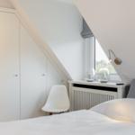Schlafzimmer mit weißem Bett, Schrank und Fenster unter Dachschräge.