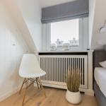 Schlafzimmer mit Bett, Stuhl und Fenster unter Dachschräge.
