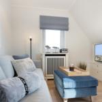 Wohnzimmer mit Sofa, blauem Sitzkissen und Fernseher.