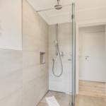 Dusche mit Glaswand, Duschbrause und Handbrause. Wanddekoration und Heizkörper sichtbar.