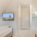 Zwei Betten, TV mit Leuchtturm-Bild, Kleiderschrank und Dachschrägen.
