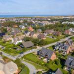 Aerial view of a coastal town with houses, greenery, and the sea in the background.