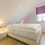 Schlafzimmer mit Doppelbett, Fenster und Nachttisch.