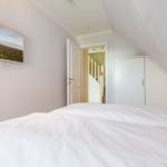 Schlafzimmer mit Dachschrägen, Bett, Kleiderschrank und Fernseher an der Wand.