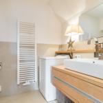 Badezimmer mit Waschmaschine, Spiegel und Waschbecken auf Holzunterschrank.