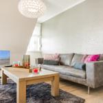 Wohnzimmer mit Sofa, Couchtisch und Fernseher. Wand mit Mosaikoptik.