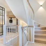 Light staircase with wooden steps and white balustrade. Left glass wall, right window with lamp.