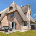 House with thatched roof and stone wall. Terrace with seating and lawn area.