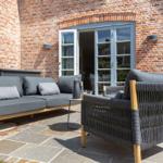 Terrace with gray sofa and chair in front of brick wall and glass door.