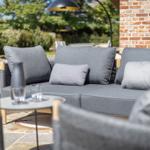 Outdoor area with gray sofa, table, and stone seating surface. Background with stone wall and trees.