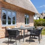 Terrace with table and chairs in front of a brick house with thatched roof.