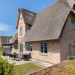 House with thatched roof and garden area with table and chairs.