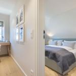 Bedroom with bed and nightstand. Adjacent room with desk and window.