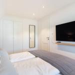 Bedroom with double bed, wardrobe, mirror, and wall-mounted TV.