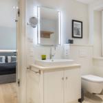 Bathroom with sink, toilet, and mirror. Bedroom with bed visible.