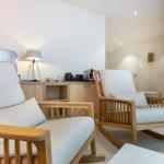 Two wooden chairs with light cushions are in a room with a cabinet and lamp.
